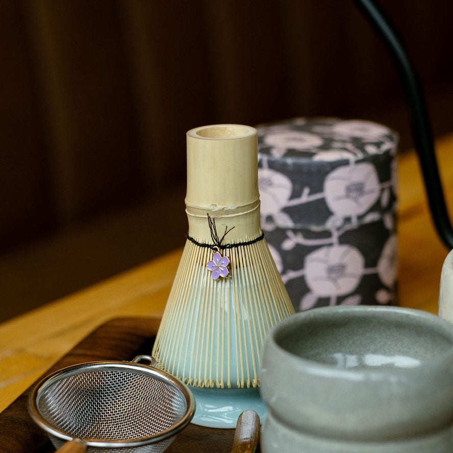 Tea-making set with bamboo whisk, tea cups, and accessories on a wooden tray.
